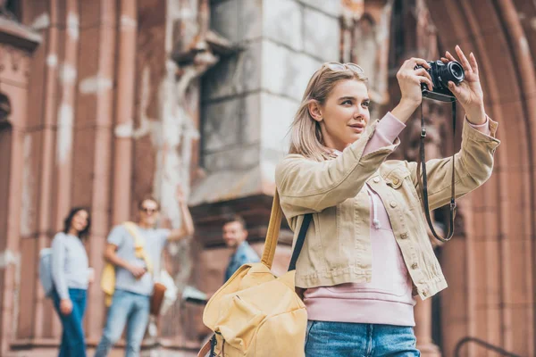 Attractive girl taking photo of city on camera with friends behind — Stock Photo
