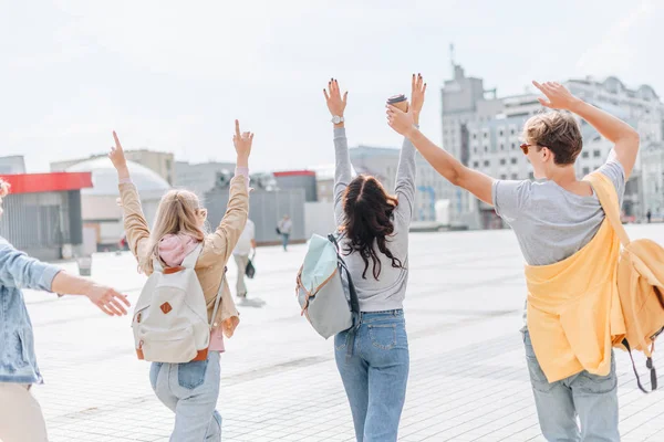 Back view of young stylish tourists waving and walking in city — Stock Photo