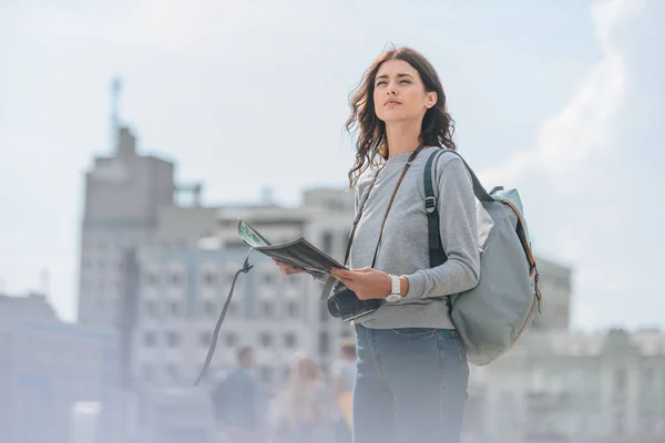 Attractive female tourist with photo camera, backpack and map walking in city — Stock Photo
