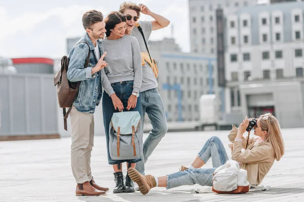 Girl sitting on street and taking photo of happy friends — Stock Photo