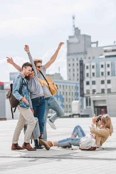 Girl sitting on street and taking photo of excited tourists in city — Stock Photo