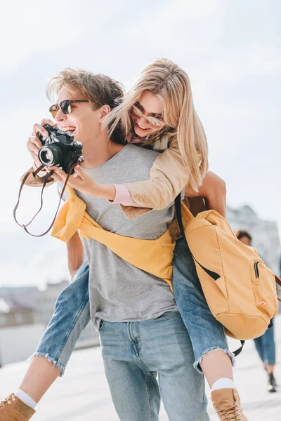 Novio dando piggyback a novia con cámara de fotos - foto de stock