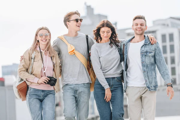 Jóvenes amigos alegres abrazando y caminando en la ciudad urbana - foto de stock