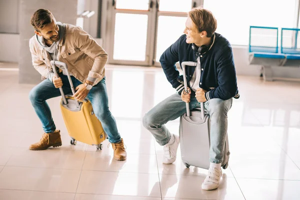 Щасливі молоді чоловіки катаються на валізах і розважаються в аеропорту — стокове фото
