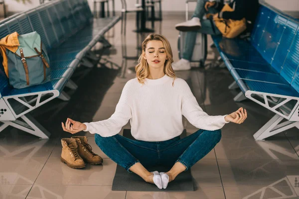 Chica meditando en posición de loto mientras espera el vuelo en la terminal del aeropuerto - foto de stock