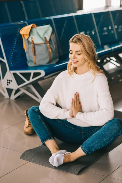 Sorrindo jovem mulher meditando na posição de lótus enquanto espera voo no terminal do aeroporto — Fotografia de Stock