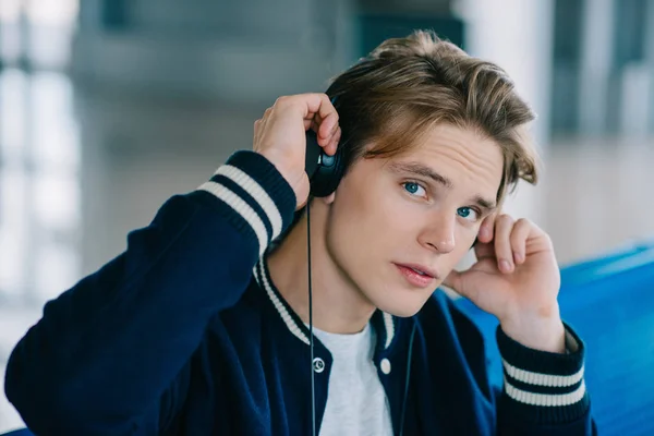 Joven guapo en auriculares mirando a la cámara mientras está sentado en el aeropuerto - foto de stock