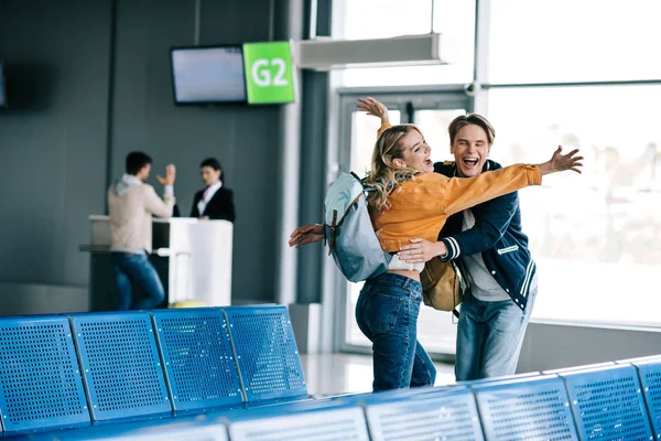 Alegre joven pareja con mochilas abrazo en aeropuerto terminal - foto de stock
