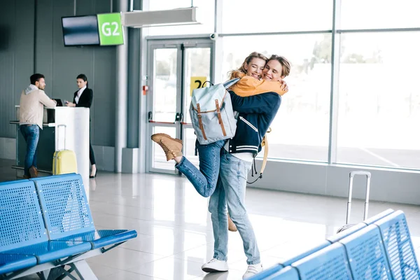 Alegre joven pareja abrazándose en aeropuerto terminal - foto de stock