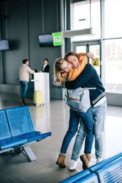 Feliz joven pareja de viajeros abrazándose en la terminal del aeropuerto - foto de stock