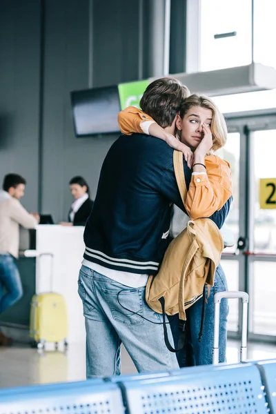 Emotional young couple hugging and girl crying in airport terminal — Stock Photo