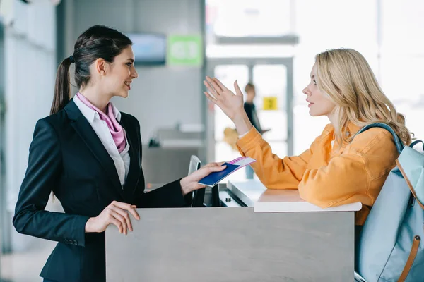 Усміхнений працівник аеропорту перевіряє документи молодої жінки-мандрівника на стійці реєстрації — стокове фото