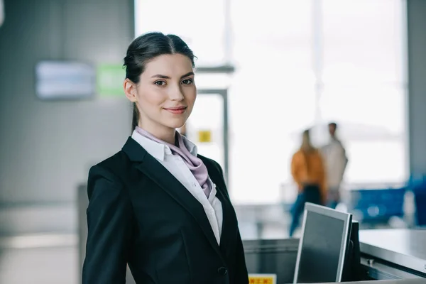 Attraktive junge Frau lächelt während ihrer Arbeit am Check-in-Schalter im Flughafen in die Kamera — Stockfoto