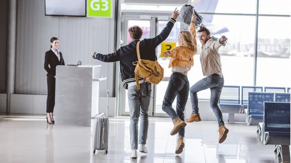 Vista trasera de jóvenes amigos emocionados corriendo al mostrador de facturación en el aeropuerto - foto de stock