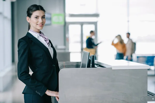 Hermosa mujer joven sonriendo a la cámara mientras trabaja en el mostrador de facturación en el aeropuerto - foto de stock