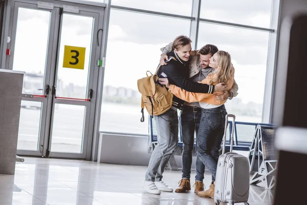 Щасливі молоді друзі обіймаються в терміналі аеропорту — стокове фото