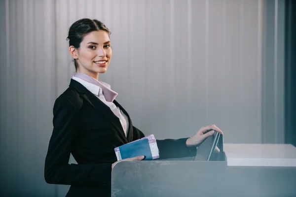 Junge Arbeiterin lächelt während ihrer Arbeit am Check-in-Schalter im Flughafen in die Kamera — Stockfoto