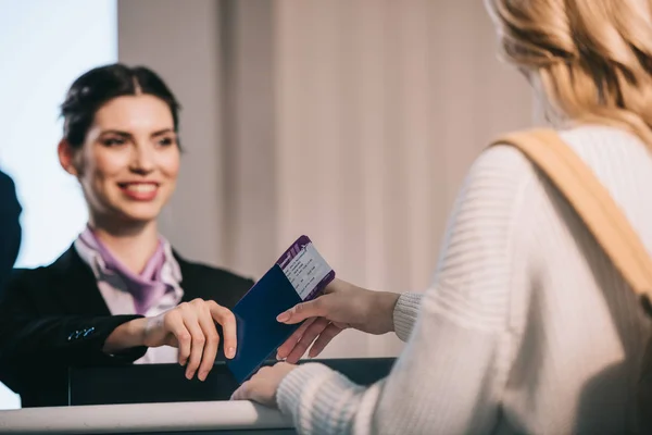 Sonriente trabajador del aeropuerto dando pasaporte con tarjeta de embarque a una joven en el mostrador de facturación - foto de stock