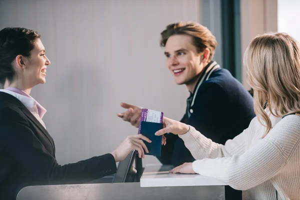 Улыбающаяся молодая пара смотрит на работника за стойкой регистрации в аэропорту — стоковое фото