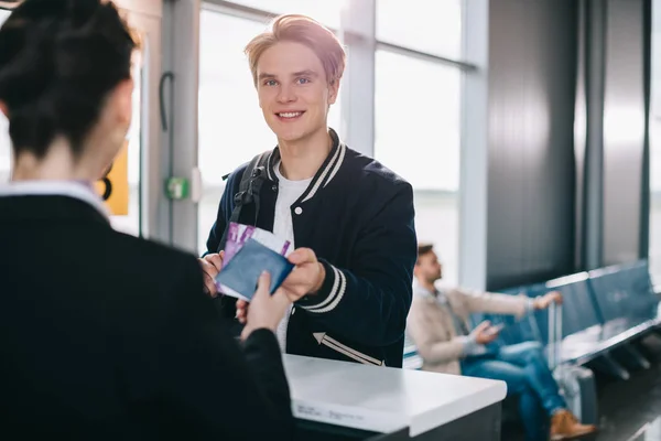Jovem sorrindo dando passaporte para o trabalhador no balcão de check-in no aeroporto — Fotografia de Stock