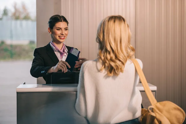 Sonriente trabajador dando pasaporte con tarjeta de embarque a una joven en el mostrador de facturación en el aeropuerto - foto de stock