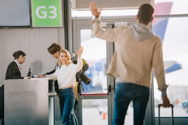 Heureux jeunes amis agitant les mains au comptoir d'enregistrement à l'aéroport — Photo de stock