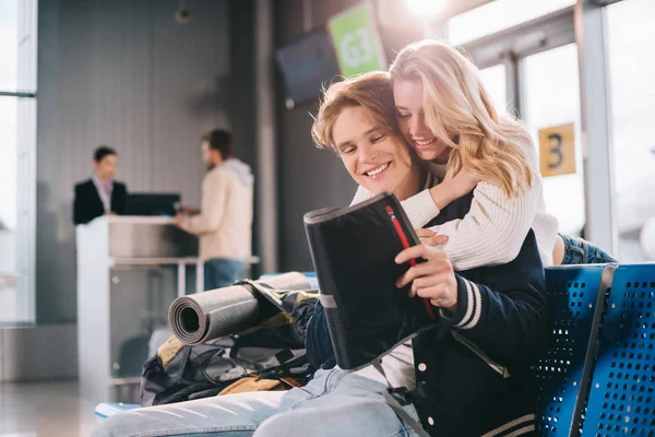 Feliz joven pareja abrazándose mientras espera en la terminal del aeropuerto - foto de stock