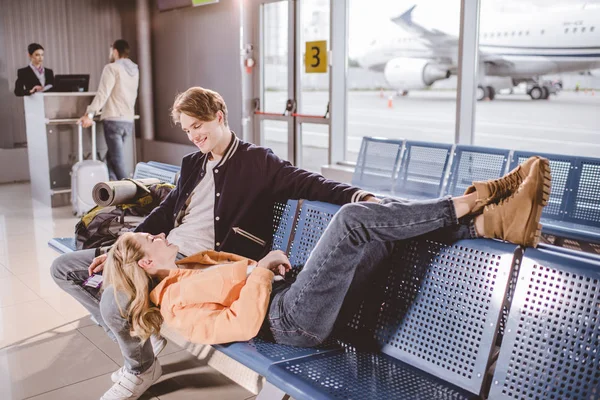 Visão de alto ângulo do jovem casal sorrindo um ao outro enquanto espera pelo voo no aeroporto — Fotografia de Stock