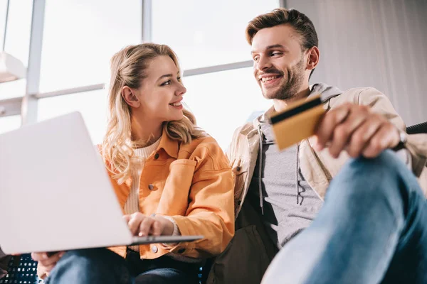 Smiling man holding credit card and young woman using laptop in airport — Stock Photo