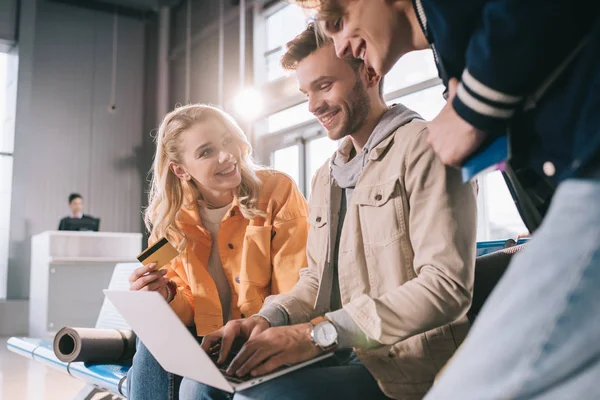 Happy friends with credit card using laptop in airport — Stock Photo