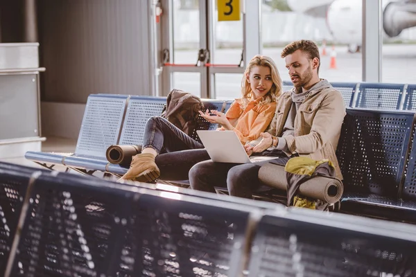 Jovem casal usando laptop e esperando voo no terminal do aeroporto — Fotografia de Stock