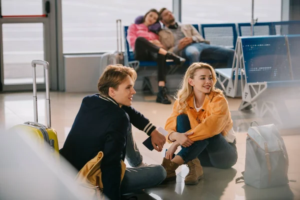 Молода пара сидить на підлозі і дивиться далеко в очікуванні польоту в аеропорту — стокове фото