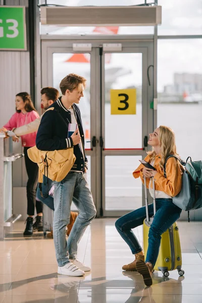 Молодой человек и женщина с паспортами и багажом разговаривают в терминале аэропорта — стоковое фото