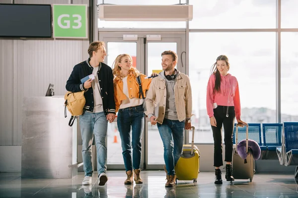 Улыбающиеся молодые друзья с документами и багажом в терминале аэропорта — стоковое фото