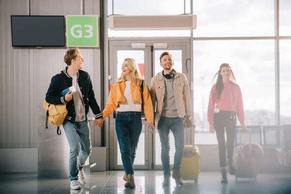 Jeunes heureux avec des documents et des bagages marchant dans le terminal de l'aéroport — Photo de stock