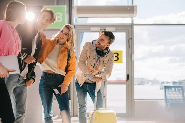 Smiling young people with documents and luggage talking in airport — Stock Photo