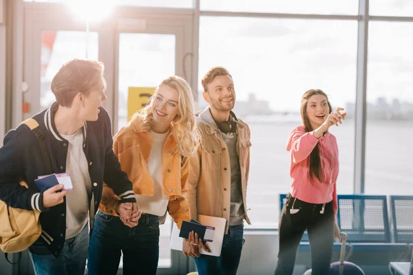 Smiling young friends holding passports, boarding passes and luggage in airport — Stock Photo