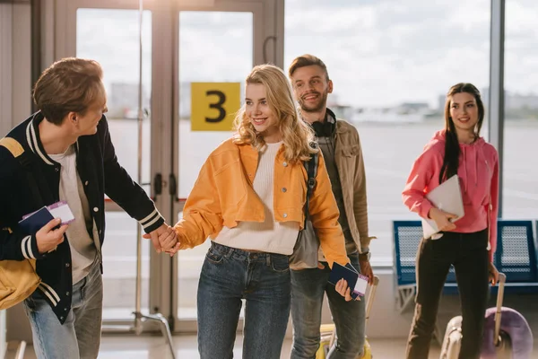 Happy young friends holding passports, boarding passes and luggage in airport — Stock Photo