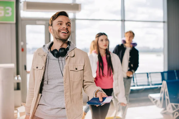 Joven sonriente sosteniendo pasaportes y tarjetas de embarque en la terminal del aeropuerto - foto de stock