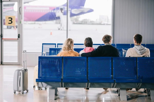Vista trasera de los jóvenes sentados y esperando el vuelo en la terminal del aeropuerto — Stock Photo