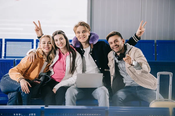 Heureux jeunes amis souriant à la caméra en attendant le vol dans le terminal de l'aéroport — Photo de stock