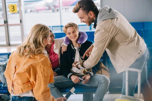 Smiling young people checking wristwatch while waiting for flight in airport — Stock Photo