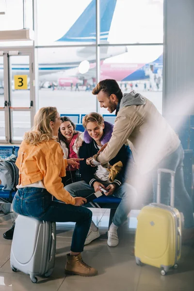 Amigos registrando el tiempo mientras esperan con el equipaje en la terminal del aeropuerto - foto de stock
