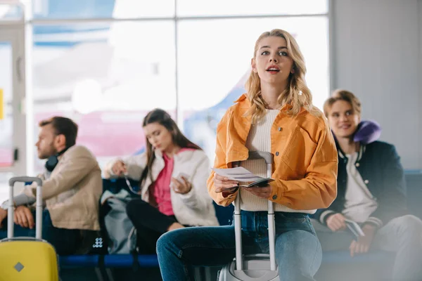 Menina com passaporte e cartão de embarque sentado em mala no aeroporto — Fotografia de Stock