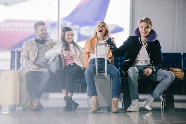 Les jeunes parlent et rient en attendant dans le terminal de l'aéroport — Photo de stock