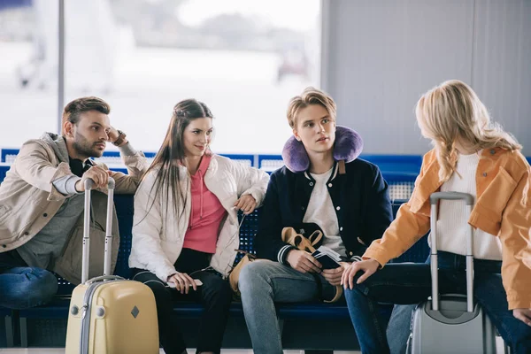 Jóvenes amigos hablando mientras esperan en la terminal del aeropuerto - foto de stock