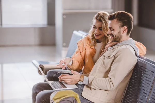 Lächelndes junges Paar benutzt Laptop beim Warten am Flughafen — Stockfoto