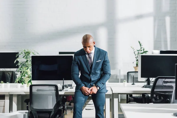 Расстроен молодой африканский американский бизнесмен сидя и глядя вниз в офисе — стоковое фото