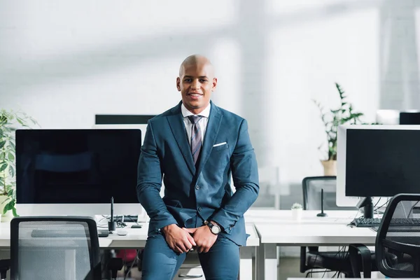 Handsome young african american businessman sitting and smiling at camera in open space office — Stock Photo