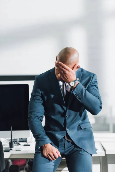 Hombre de negocios afroamericano cansado sentado con la mano en la frente en el lugar de trabajo - foto de stock